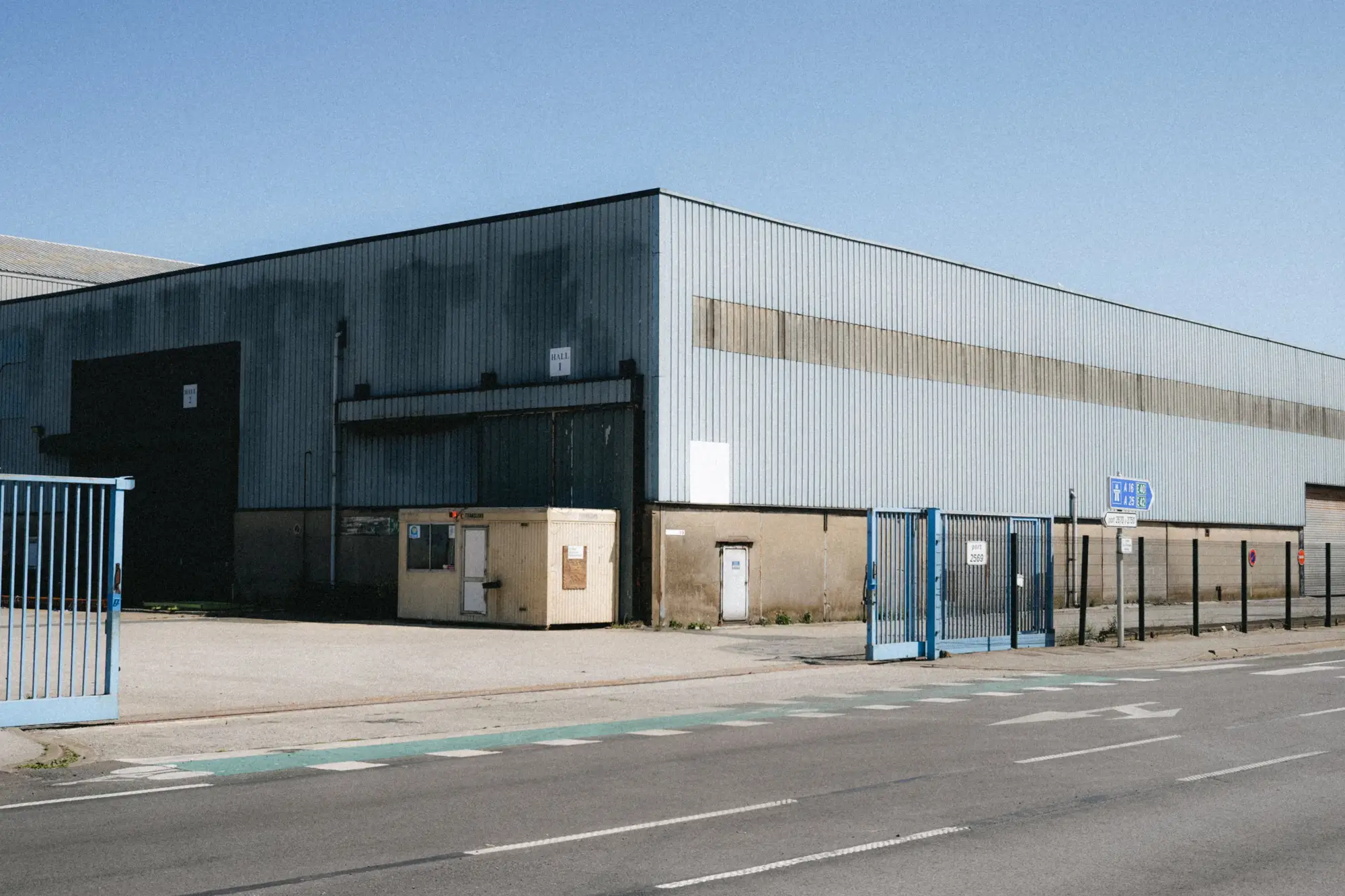 The gate and yard of a metal-clad warehouse seen from the road