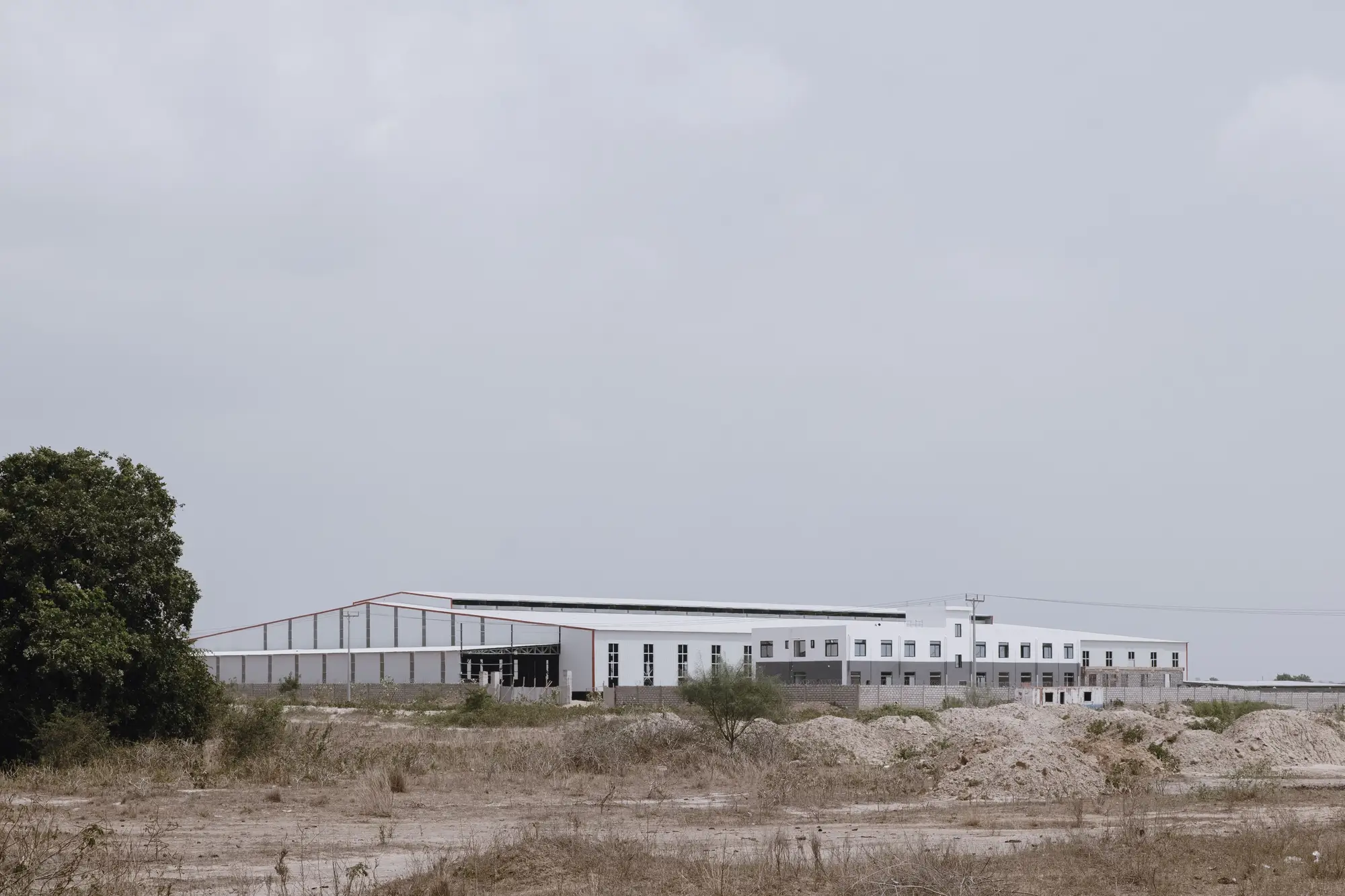 A long, low industrial plant standing alone on open ground under an overcast sky